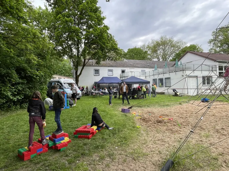Kinder balancieren auf Spielgeräten auf der Wiese, im Hintergrund Pavillons und das Vereinsheim
