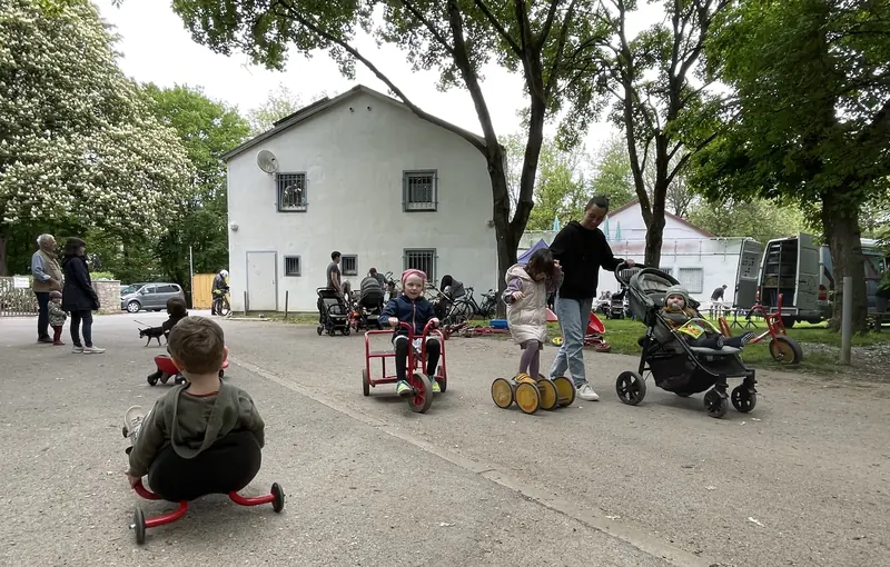 Kinder fahren mit Rollern und Dreirädern auf dem Platz vor dem Vereinsheim