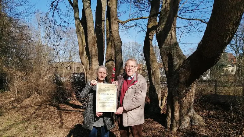 Anne Heß-Willner und Dr. Wolfgang Rebstöck halten unter einem alten, mehrstämmigen Baum eine gerahmte Urkunde